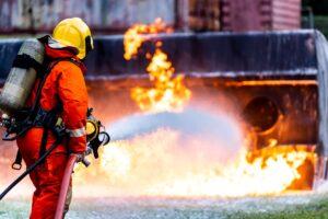 A firefighter putting out a raging fire at a plant with a foam extinguisher.