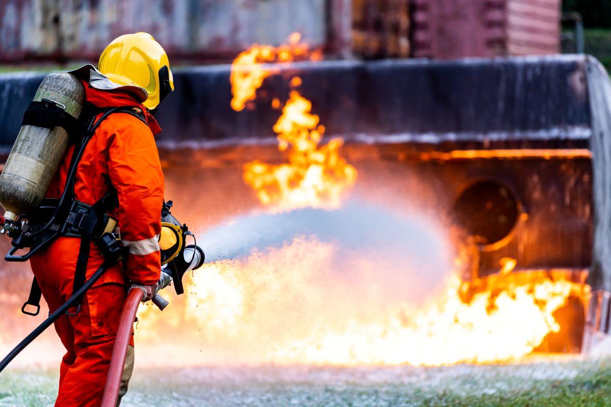 A firefighter putting out a raging fire at a plant with a foam extinguisher.