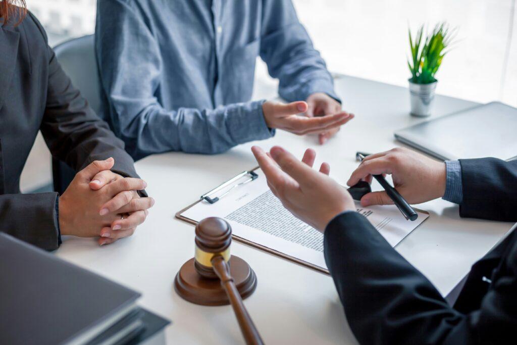Lawyer meeting with clients at a desk, discussing legal documents placed beside a gavel and clipboard during a consultation.
