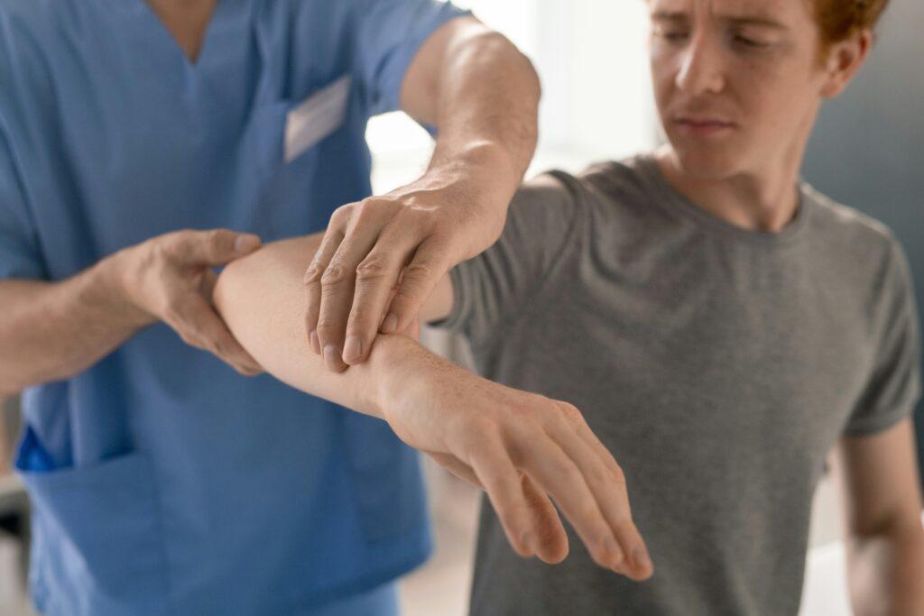 Doctor examining a patient’s injured arm, gently rotating and assessing movement while the patient reacts with discomfort.