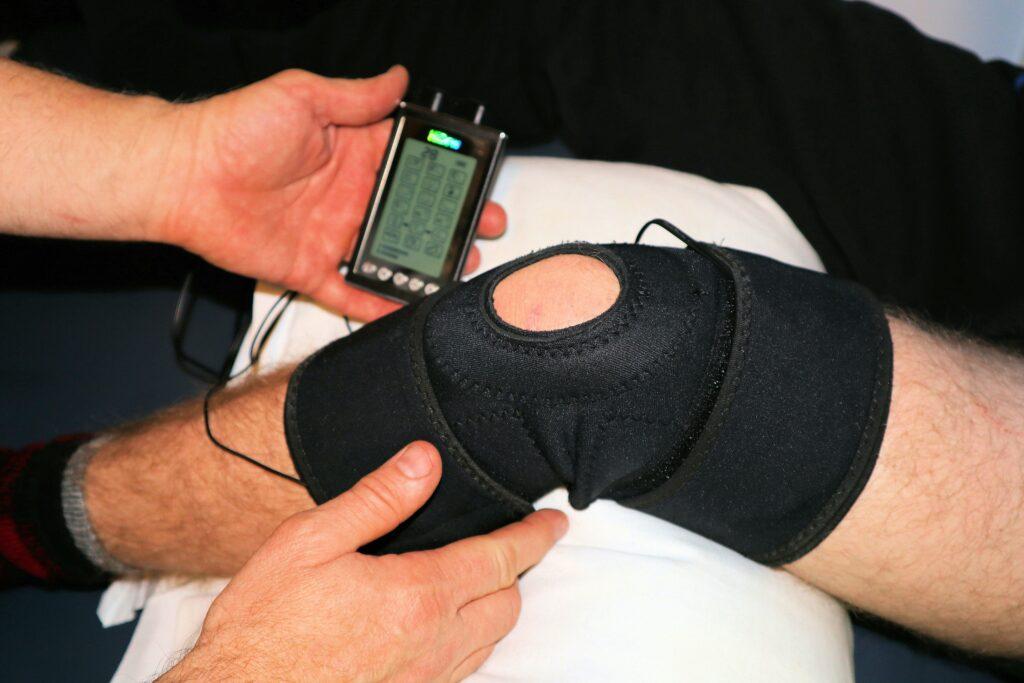 Close-up of a person receiving knee therapy with a brace and electronic stimulation device during rehabilitation.