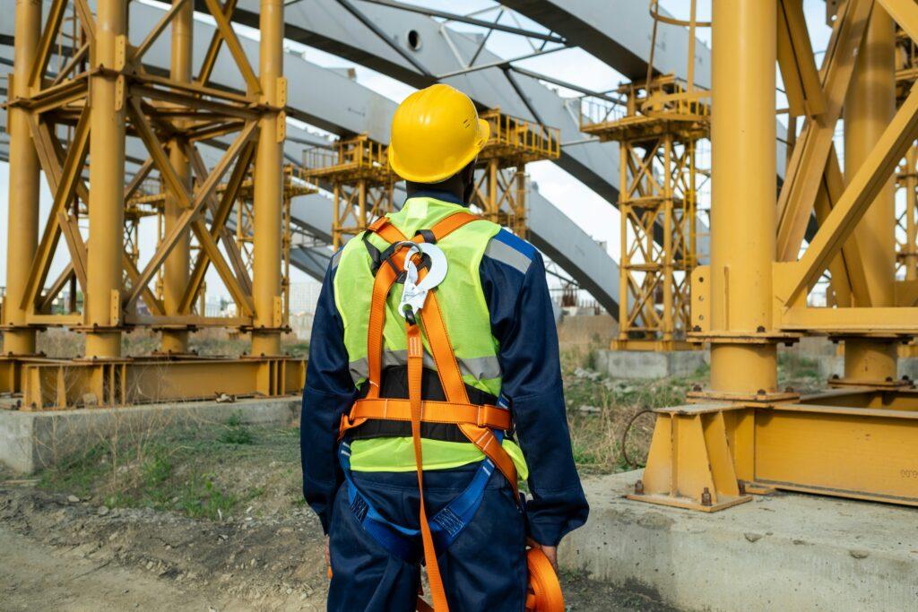 A man in safety gear stands in front of a large construction site, overseeing the ongoing building project.