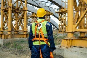 A man in safety gear stands in front of a large construction site, overseeing the ongoing building project.