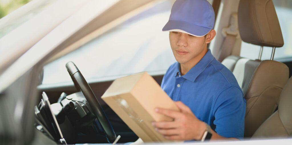 A delivery man in a car holds a box, ready to make a delivery.