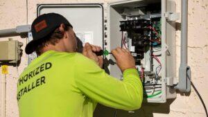 A man in a green shirt repairs an electrical panel, focused on ensuring proper functionality and safety.