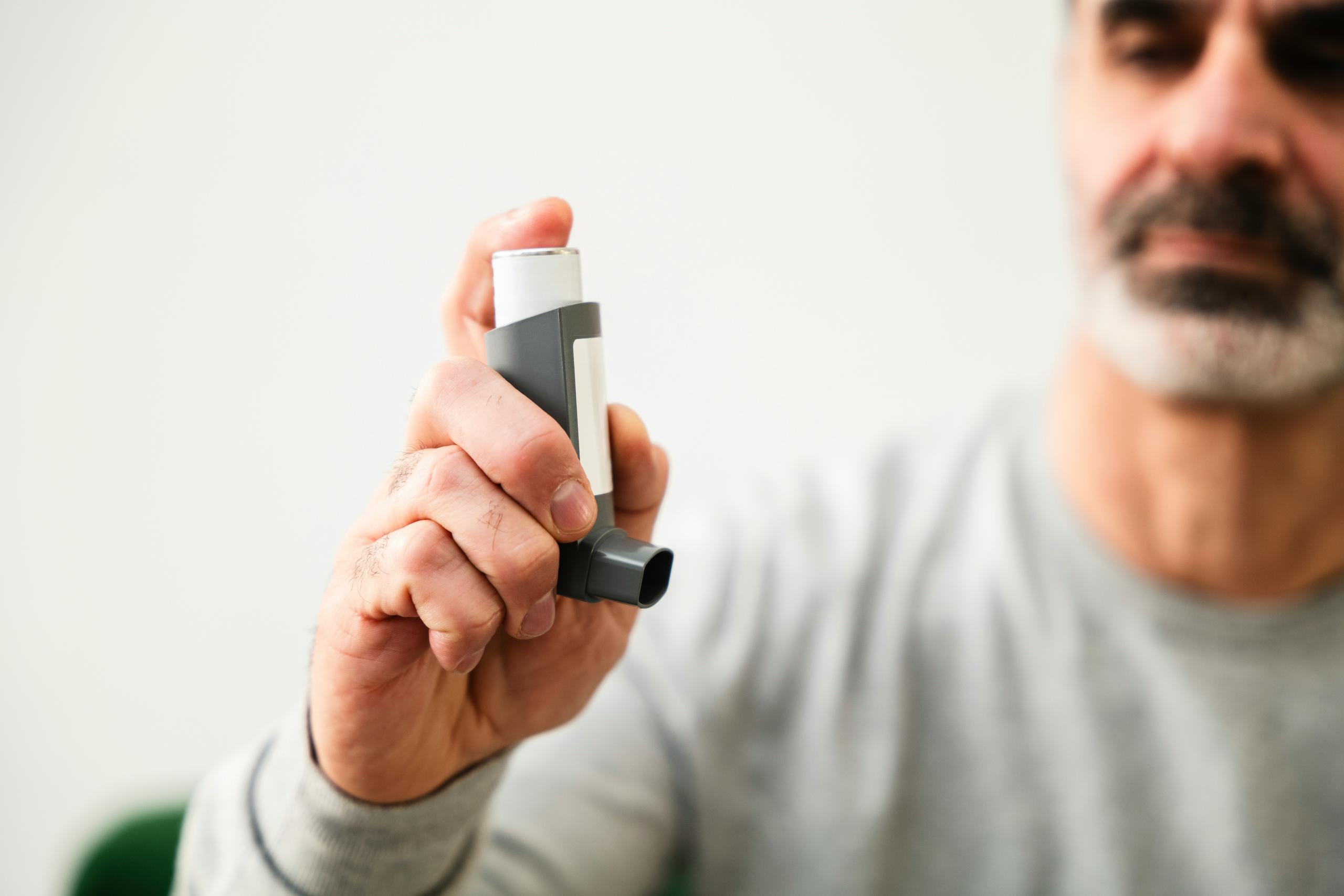 A man holding an inhaler in his right hand, looking focused and ready to use it.