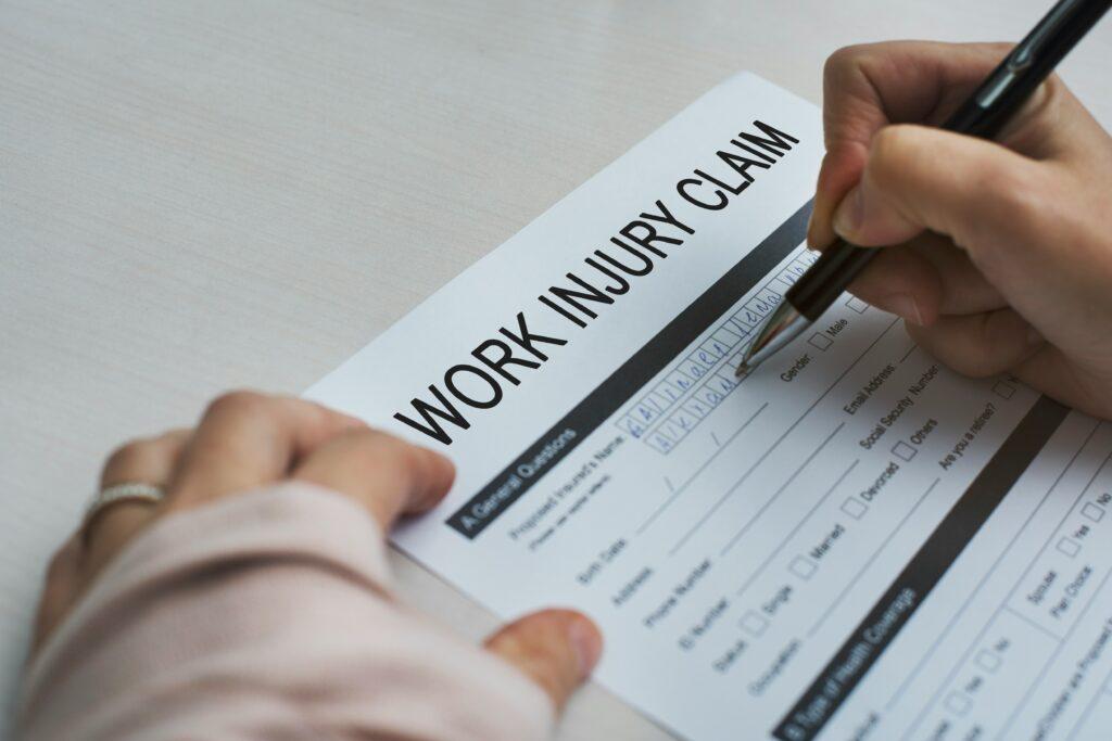 A person filling out a work injury claim form at a desk, focused on providing detailed information.
