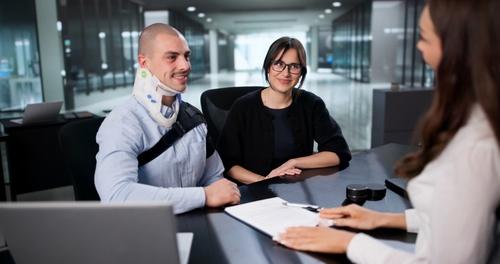 Worker wearing neck brace meeting with attorney across desk beside companion