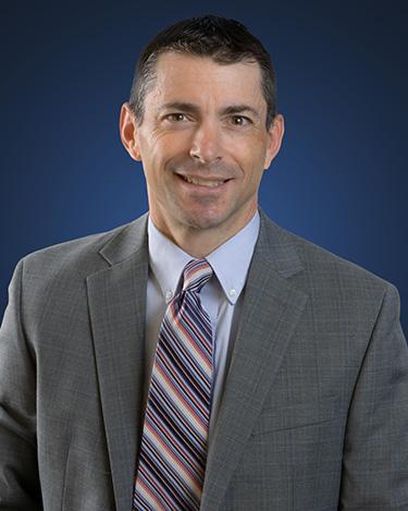 Attorney Lou D'Onofrio, in front of a blue background wearing a grey suit