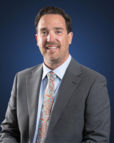 Ryan Hauck, wearing a grey suit in front of a blue background