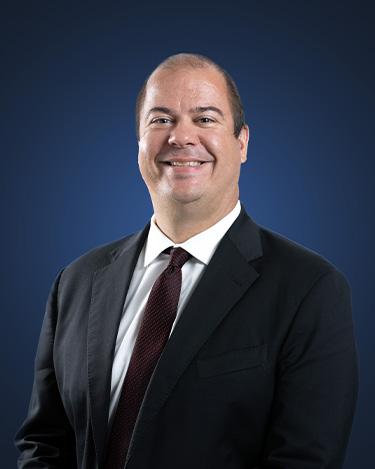 Attorney Andrew Shumlas wearing a dark suit in front of a dark blue background