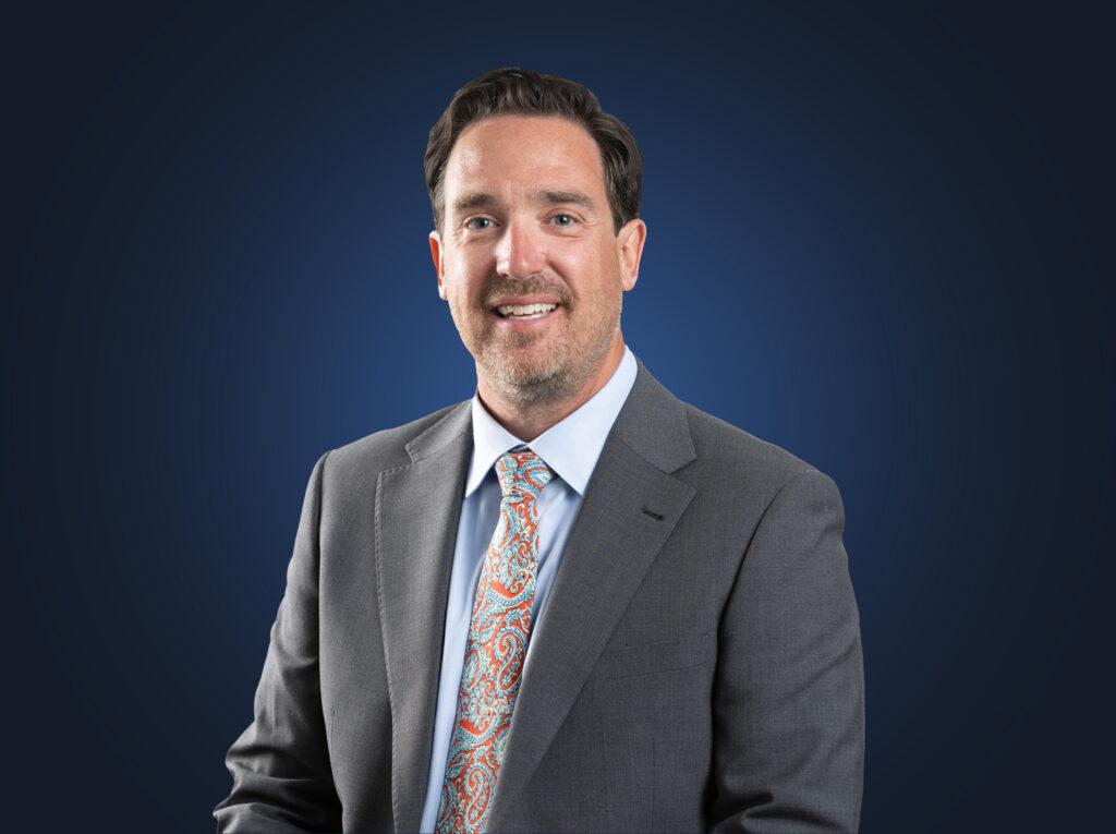 Attorney Ryan Hauck wears a grey suit in front of a blue background