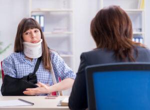 Woman wearing a neck brace and arm sling talking with another person across a desk