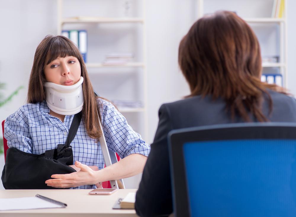 Woman wearing a neck brace and arm sling talking with another person across a desk