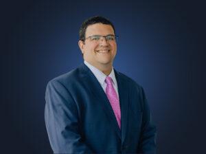 Attorney Brian Dunstone wears a dark suit and pink tie in front of a dark background