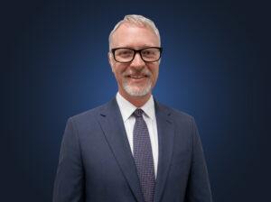 Attorney Jonathan Elms, wearing a dark suit in front of a dark blue background
