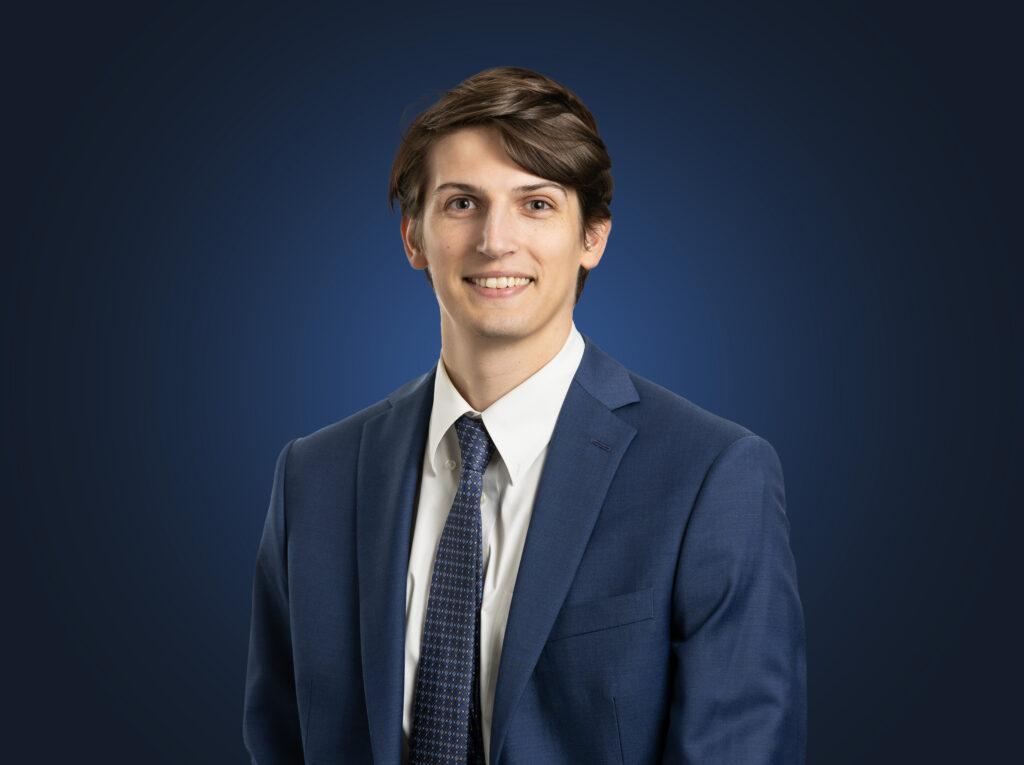 Carter Davis wearing a dark suit in front of. a dark blue background